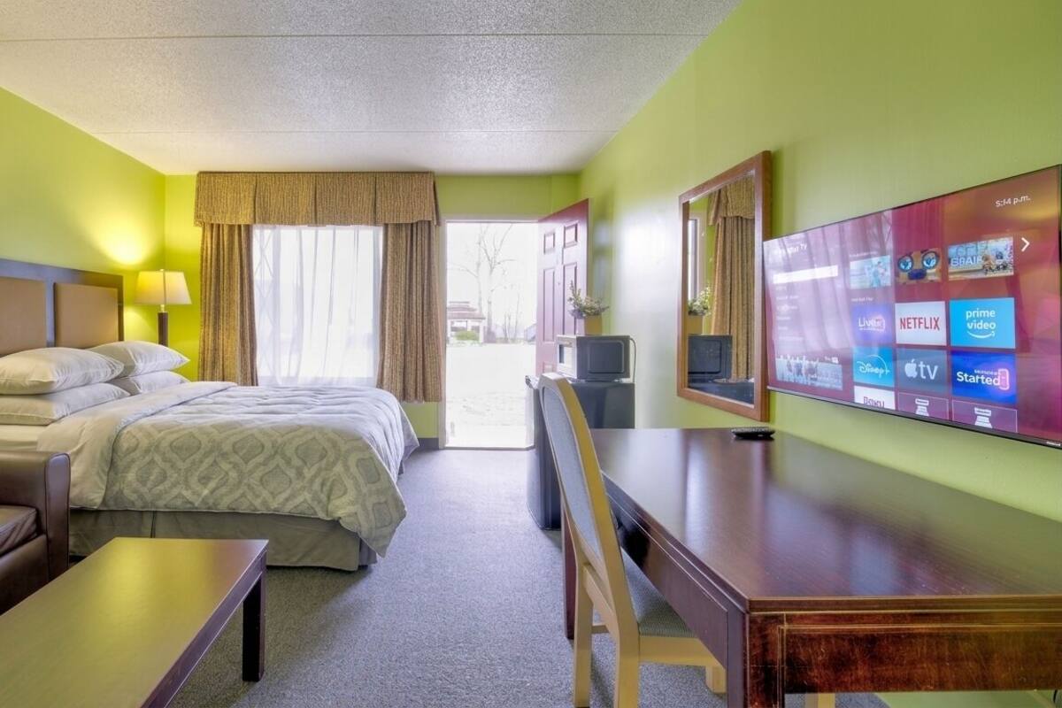 A hotel room with a bed, a desk, a chair, a TV, and a window with curtains.