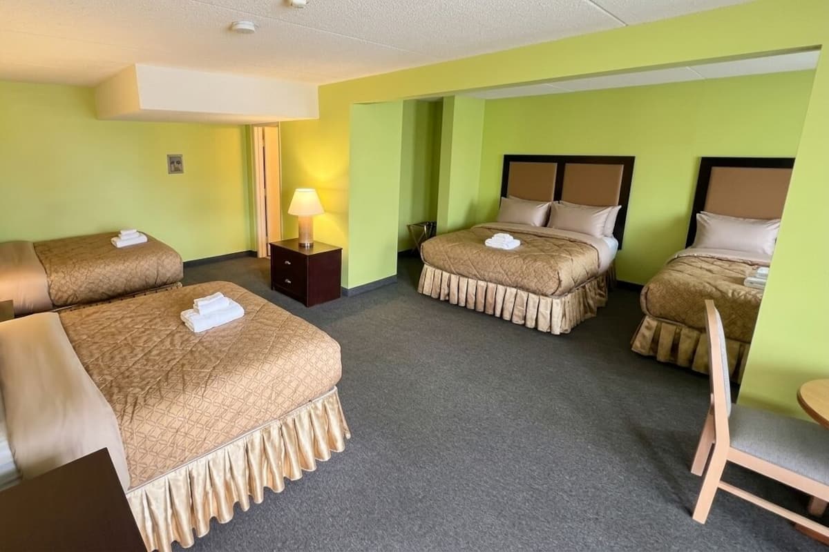 A hotel room with two beds, a desk, a chair, and a lamp.