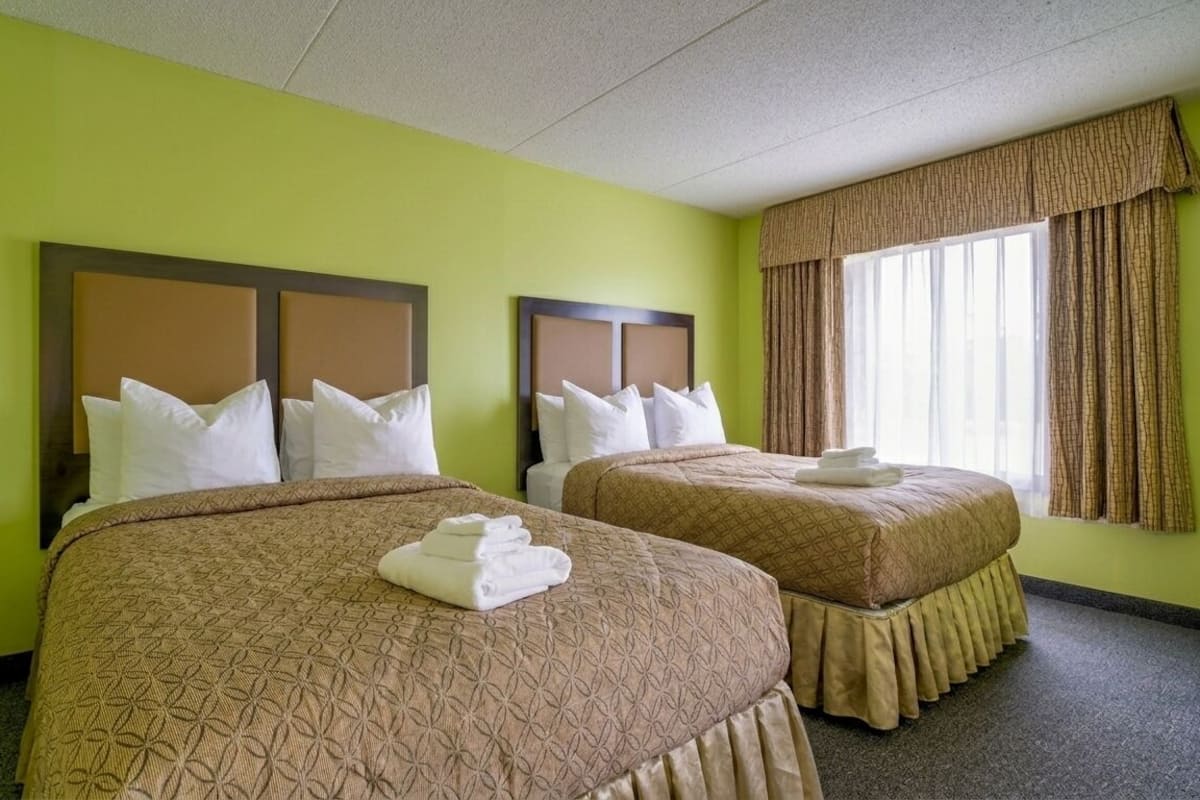 A hotel room with two beds, a window with curtains, and a green wall.