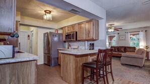 A kitchen with wooden cabinets, a refrigerator, a microwave, and a coffee maker. There is a dining area with chairs and a sofa. - Lakeview Escape Kayaks (Inverness)