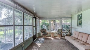 A sunroom with large windows, a beige sofa, and two patterned chairs. - Lakeview Escape Kayaks (Inverness)