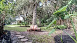 A garden with a wooden bench, stepping stones, and a large tree with hanging moss. - Lakeview Escape Kayaks (Inverness)