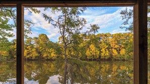 A wooden deck with a view of a lake surrounded by trees reflecting in the water.