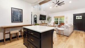 A modern kitchen with a central island, wooden cabinets, and a dining area with a sofa and chairs.