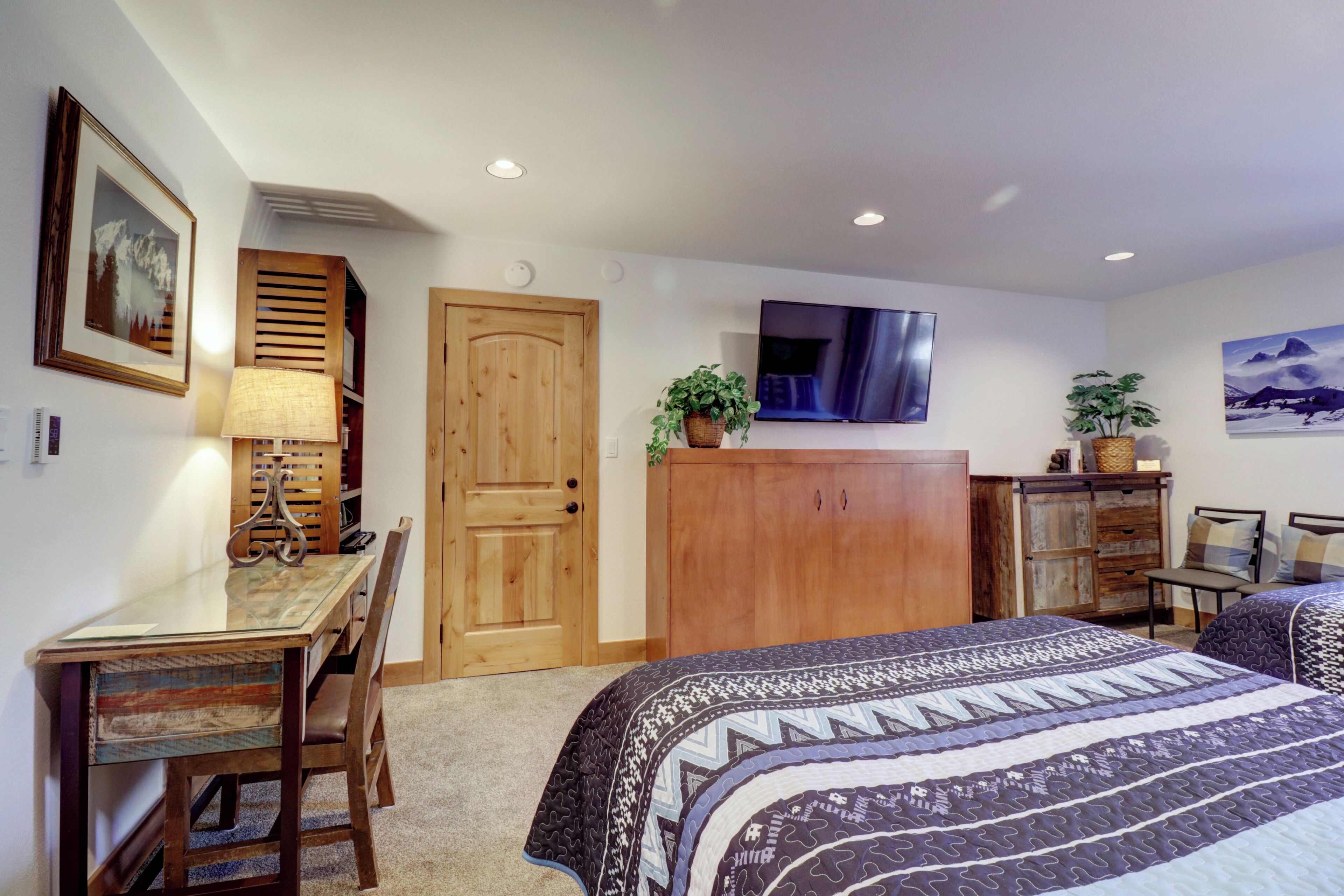 A bedroom with a bed, a desk, a chair, a wardrobe, a television, and a door.