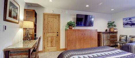 A bedroom with a bed, a desk, a chair, a wardrobe, a television, and a door.