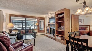 A cozy living room with a fireplace, a large wooden bookshelf, and a dining area with a table and chairs.