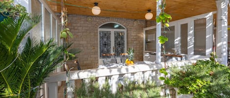A covered outdoor dining area with a brick wall, wooden ceiling, and hanging plants.