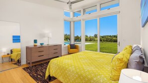 A bedroom with a large bed, a ceiling fan, a dresser, and a view of a swimming pool.