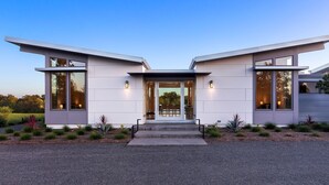 A modern two-story house with a flat roof, large windows, and a covered entrance.