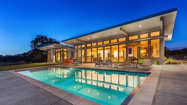 A modern house with a swimming pool, outdoor seating, and large windows.