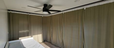 A room with a ceiling fan, large curtains, and a window with blinds.