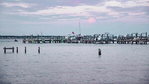 Un muelle frente al agua con barcos amarrados, una bandera y mar en calma.