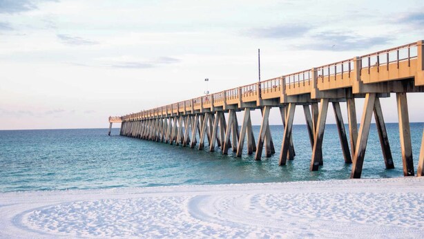 Un muelle que se adentra en un mar tranquilo, con una playa arenosa al final.
