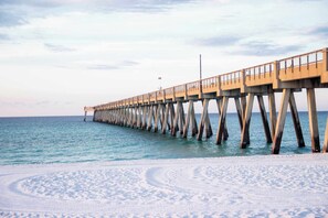A pier extending into a calm sea with a sandy beach at its end.