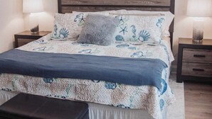 Un dormitorio con cama, dos mesitas de noche, una lámpara de noche, un espejo decorativo y un ventilador de techo.