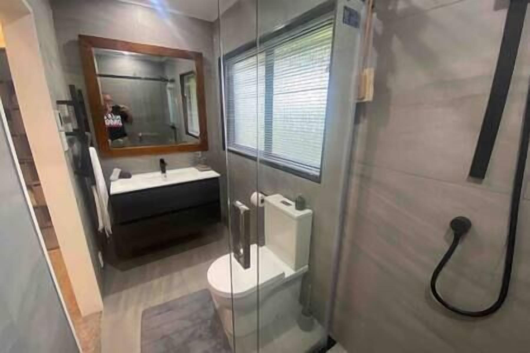 A modern bathroom with a glass shower enclosure, a vanity with a mirror, and a toilet.