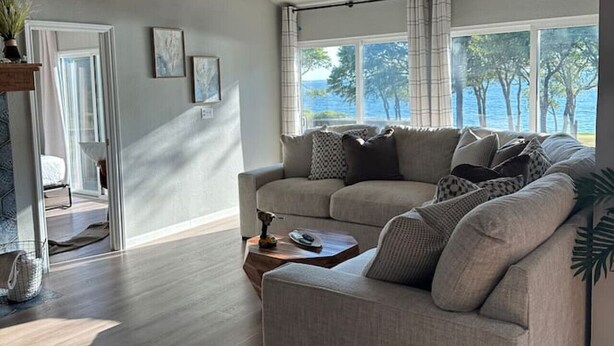 Un salón moderno con un sofá gris, una mesa de centro y vistas al mar a través de grandes ventanales.