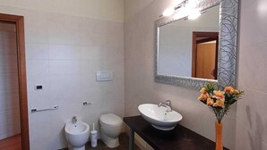 Een badkamer met een wastafel, toilet, bidet en een spiegel met verlichting.