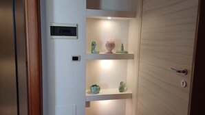 Een hal met een houten deur, een intercom op de muur en planken met decoratieve objecten.