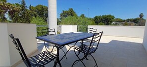 Eine Dachterrasse mit Tisch und Stühlen, umgeben von einer weißen Mauer und Grünpflanzen.
