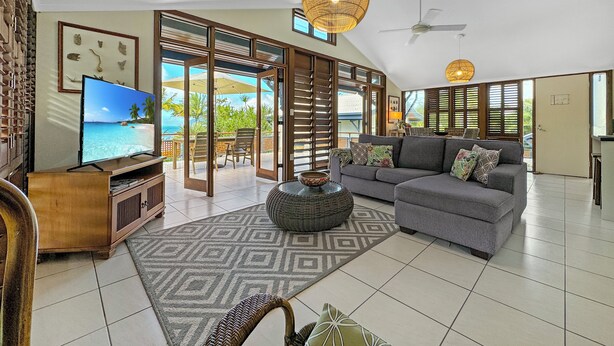 A spacious living room with a large flat-screen TV, a grey sofa, and a patterned rug. - Wongalinga Beachfront Apt 4 (Wongaling Beach)