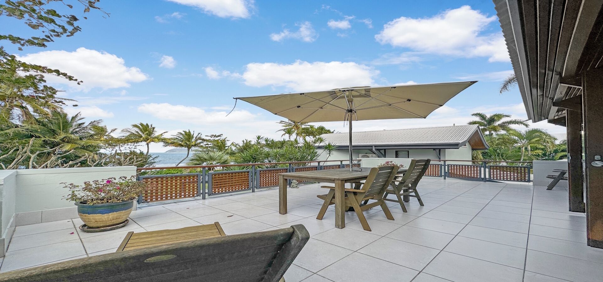 A patio with a table and chairs, a large umbrella, and a view of the ocean.