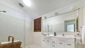 A modern bathroom with a large mirror, two sinks, a shower, and a wicker basket. - Wongalinga Beachfront Apt 4 (Wongaling Beach)