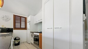 A compact kitchen with white cabinets, a microwave, an oven, and a refrigerator. - Wongalinga Beachfront Apt 4 (Wongaling Beach)
