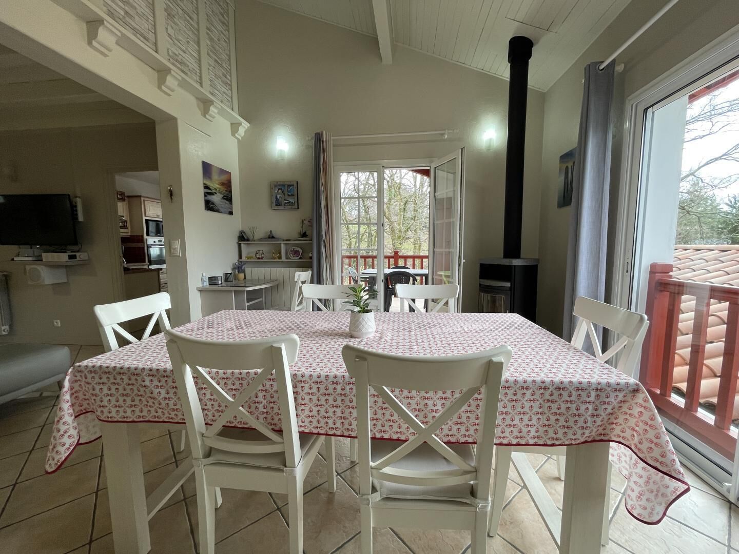 A dining area with a table covered in a patterned tablecloth, surrounded by white chairs.