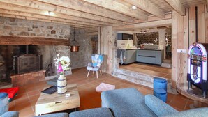 A rustic interior with a stone fireplace, a small kitchen, and a seating area with a blue sofa and armchairs. - 4 bedroom nice home in Saint Etienne de Serre (Saint Etienne de Serre)