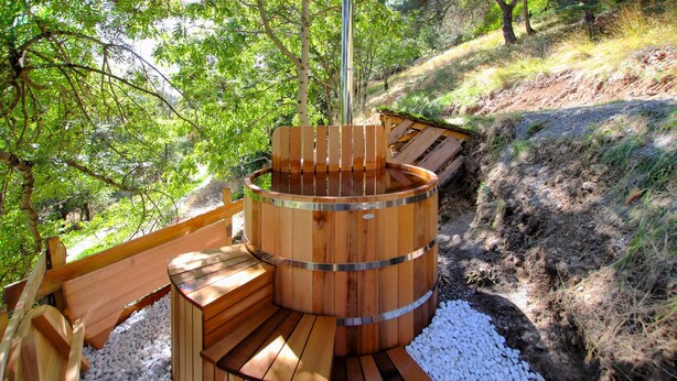 A wooden hot tub with a bench, surrounded by gravel and trees. - 4 bedroom nice home in Saint Etienne de Serre (Saint Etienne de Serre)