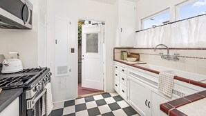 A compact kitchen with a gas stove, microwave, and a checkered floor. - Enjoy indoor-outdoor living, a full kitchen, and vintage coastal charm. (Santa Barbara)