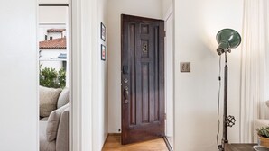 A hallway with a dark wooden door, a floor lamp, and a couch in the background. - Enjoy indoor-outdoor living, a full kitchen, and vintage coastal charm. (Santa Barbara)