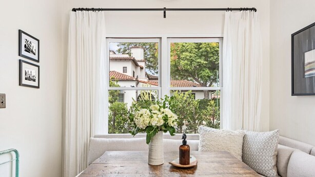 A cozy room with a large window, a wooden table with a vase of flowers, and a sofa with cushions. - Enjoy indoor-outdoor living, a full kitchen, and vintage coastal charm. (Santa Barbara)