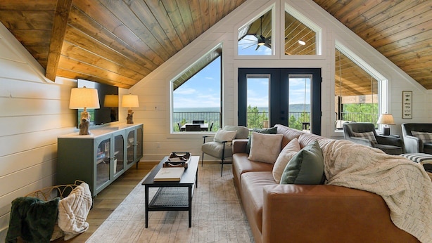 A spacious loft with a high ceiling, large windows, and a cozy seating area with a couch and chairs. - Breathtaking Mountain Views-Hot Tub/Luxe Firepit/Daybed Swing & Slide- New Cabin (Broken Bow)