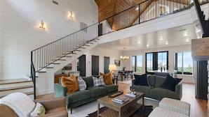 A spacious living area with a staircase, green sofas, and a dining area. - Breathtaking Mountain Views-Hot Tub/Luxe Firepit/Daybed Swing & Slide- New Cabin (Broken Bow)