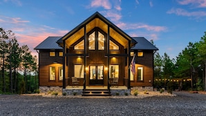 A large, two-story log cabin with a prominent front porch and a stone foundation. - Breathtaking Mountain Views-Hot Tub/Luxe Firepit/Daybed Swing & Slide- New Cabin (Broken Bow)