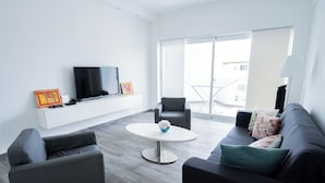A modern living room with a flat-screen TV, grey sofas, a round coffee table, and a balcony with a railing. - Baya Azul Bayahibe - Penthouse 401 (San Rafael del Yuma)