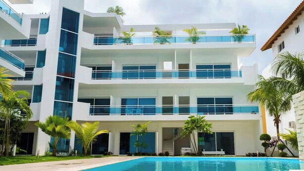 A modern multi-story building with a swimming pool in front. - Baya Azul Bayahibe - Penthouse 401 (San Rafael del Yuma)