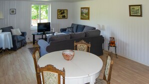Un salon comprenant un ensemble de canapés, un téléviseur, une table à manger avec des chaises et des tableaux encadrés accrochés aux murs.