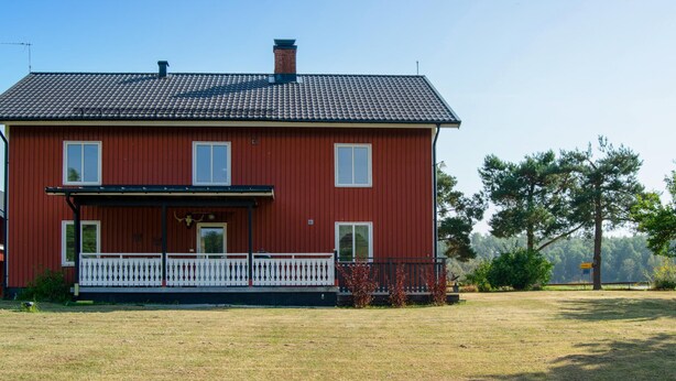 Une maison rouge à deux étages, dotée d’un balcon et d’une cour avant clôturée.