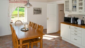 Une salle à manger avec une table et des chaises en bois, une cuisine avec des meubles blancs et une fenêtre donnant sur un paysage verdoyant.