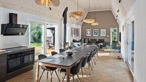 Una cocina moderna con estufa integrada, un comedor con una mesa larga y sillas, y un rincón de descanso acogedor con chimenea.