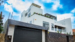 A modern two-story building with a large garage door, a flat roof, and a balcony with plants. - Luxury seaside villa (Ngaparou)