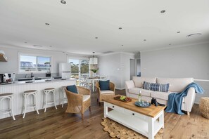 A modern kitchen with white cabinetry, a dining area with white chairs, a wooden coffee table, and a sofa with a blue throw. - Bawley Blue Pet Friendly at Bawley Point (Bawley Point)