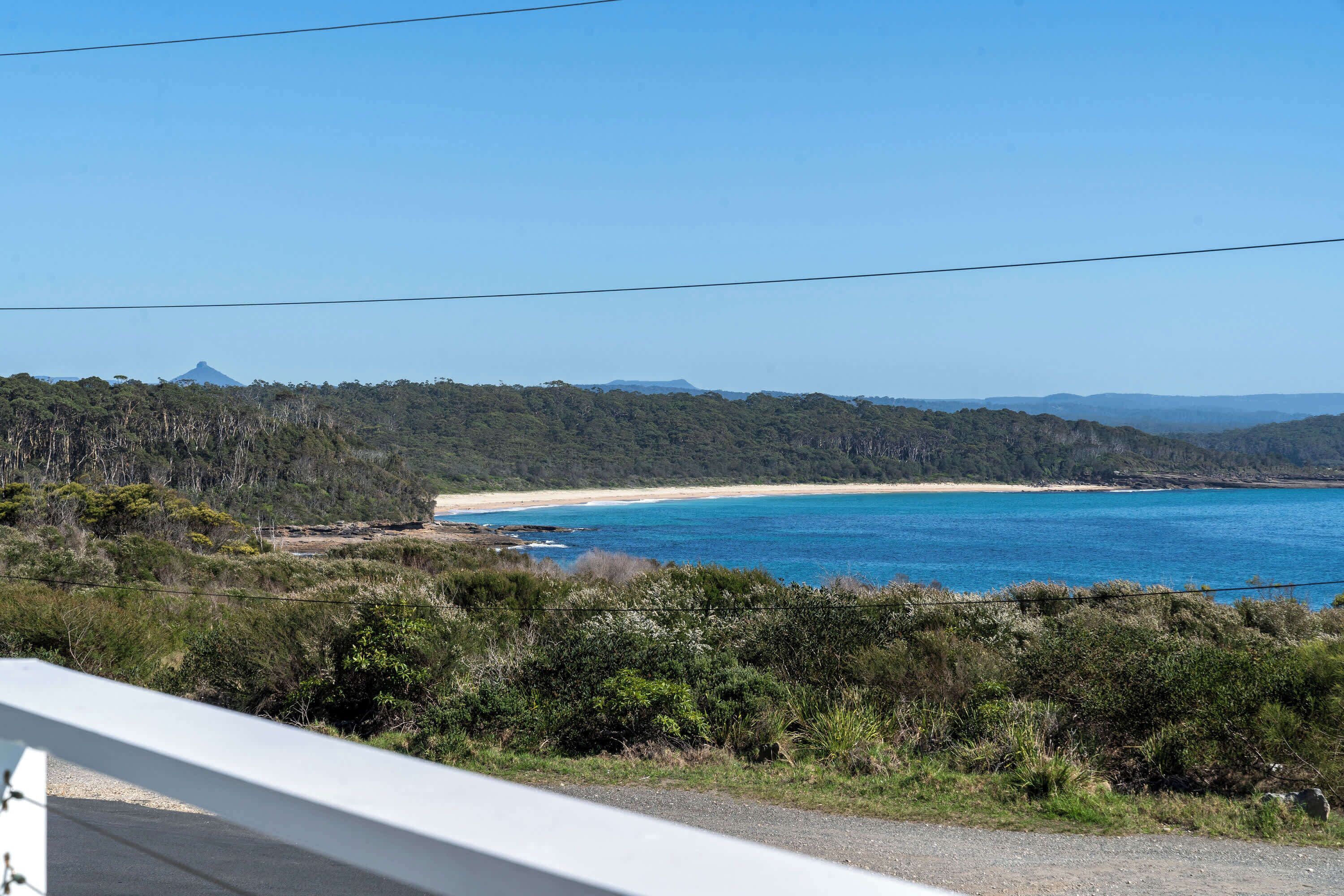Eine Küstenlandschaft mit Strand, bewaldeten Hügeln und wolkenlosem Himmel.