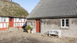 A traditional building with a thatched roof and a grey tiled roof, a white bench, and a cobblestone courtyard. - Awesome home in Randers SV with WiFi (Randers SV)