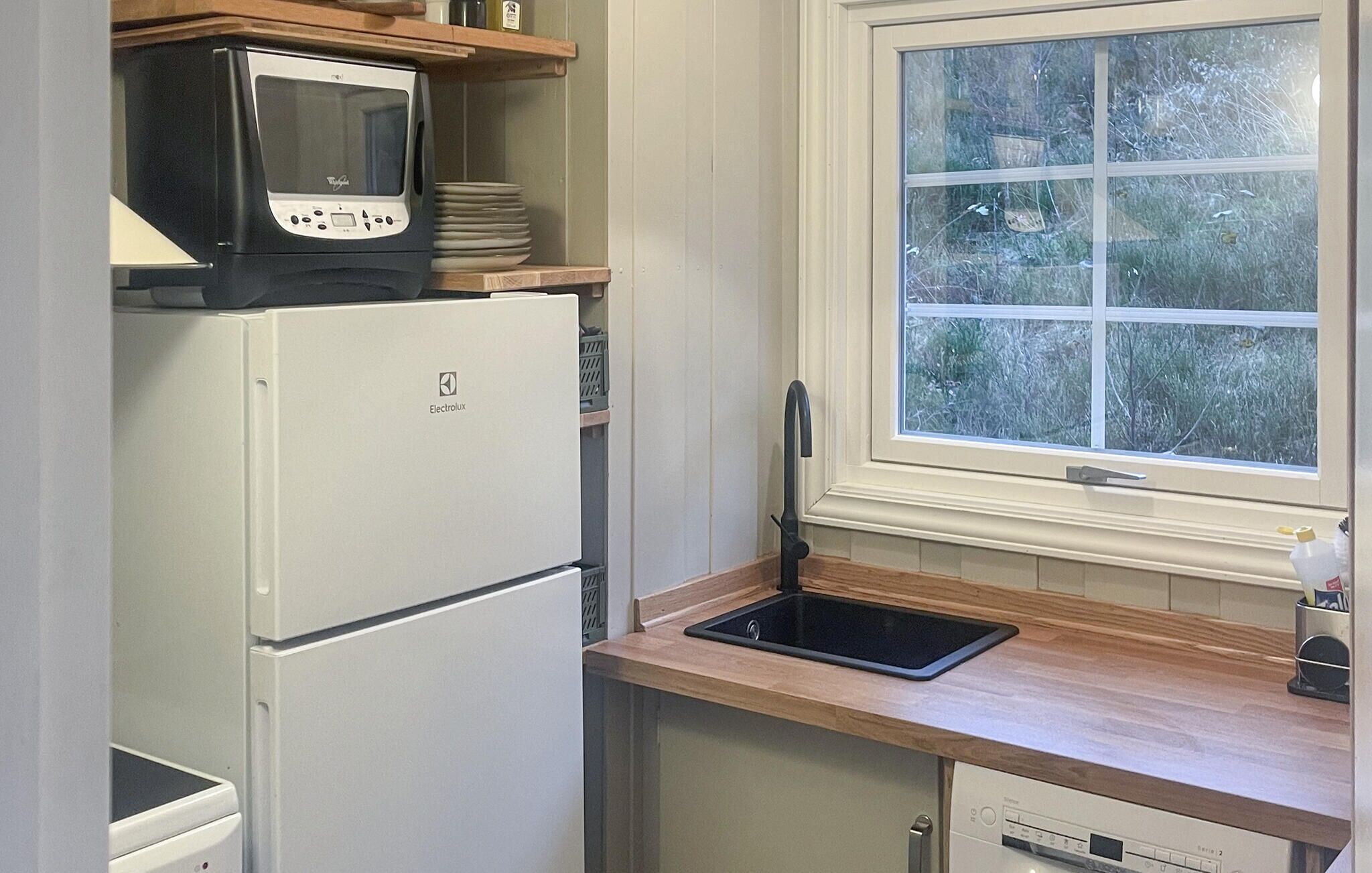 Een kleine keuken met een witte Electrolux koelkast, een zwarte magnetron en een gootsteen met een zwart aanrecht.