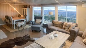 A spacious living room with a large window offering a mountain view, a dining area with a table and chairs, and a cozy seating area with a sofa and armchairs. - 4 bedroom cozy home in Bø i Telemark (Bø i Telemark)